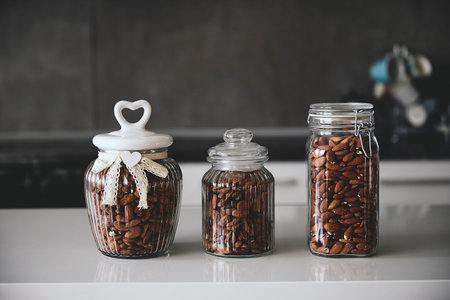 Three elegant glass jars filled with whole almonds sit on a modern kitchen counter, showcasing...