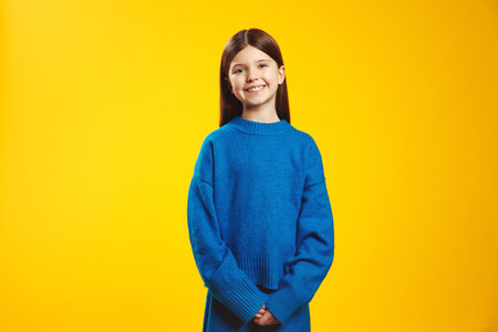 Joyful youngster wearing a cozy blue sweater, standing confidently with a cheerful smile on a vivid yellow background. Perfect for children fashion ads and cheerful marketing materials.の写真素材