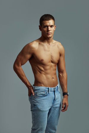 Confident shirtless man models against a blue background, emphasizing fitness, youth, and style. Highlighting strength and fashionable casual wear against grey backgroundの写真素材