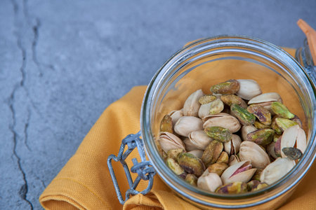Many natural pistachios in glass bowl on gray background cracked concrete.