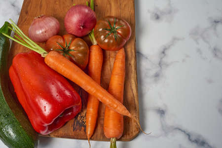 Various greens and vegetables on wooden kitchen table a white marble surface. Carrots, peppers, zucchini, tomatoes and onionsの写真素材