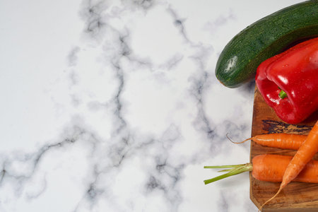 Various greens and vegetables on wooden kitchen table a white marble surface. Carrots, peppers, zucchini, tomatoes and onions. With space for text.の写真素材