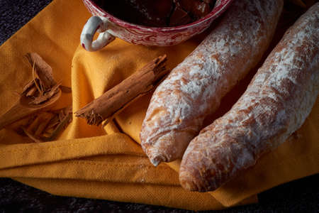 Fartons, typical pastries from Valencia, Spain, with hot chocolate, in a Chinese ceramic container on top of a yellow cloth, with a dark surface. A sweet breakfast or snack.の写真素材