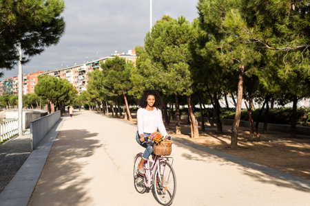 Black happy young woman riding a vintage bicycle with beautiful basket of flowers