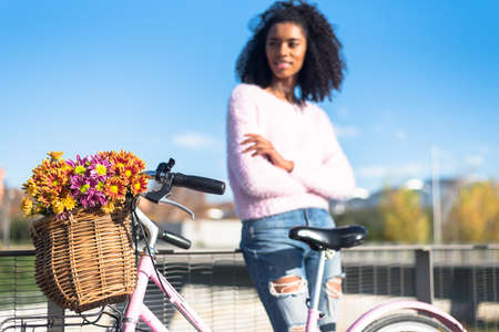 Black happy young woman enjoying a sunny day by the river with her vintage bicycle with a beautiful basket of flowersの写真素材