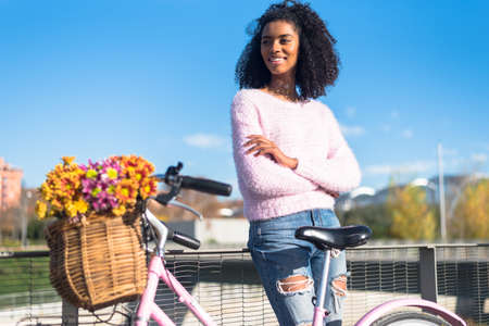 Black happy young woman enjoying a sunny day by the river with her vintage bicycle with a beautiful basket of flowersの写真素材