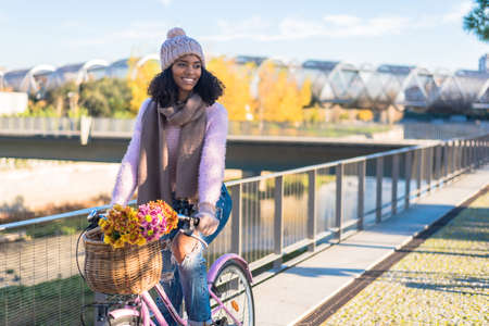 Black young woman riding a vintage bicycle with flowers の写真素材