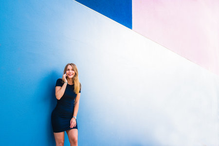 Happy young woman on the mobile phone by a colorful wallの写真素材