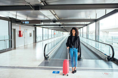 black woman in the moving walkway at the airport with a pink suitcase.の写真素材