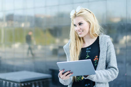 happy blonde student woman with tablet in a reflection wallの写真素材