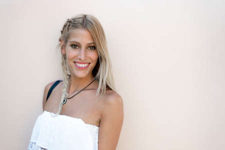 happy blonde woman smiling looking at the camera in a cream color wall.の写真素材