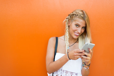 Happy blonde woman in a orange background wall using a mobile phone.