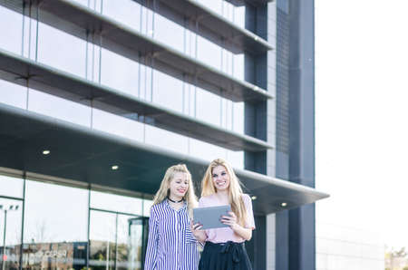 two blonde students friends laughing using mobile phone and tabletの写真素材