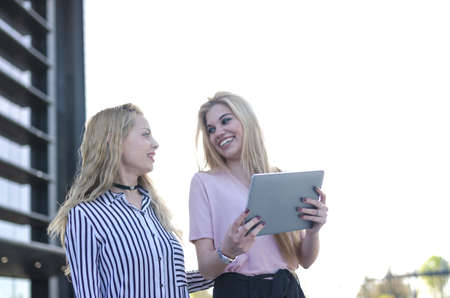 two blonde students friends laughing using mobile phone and tabletの写真素材
