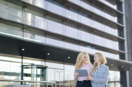 two blonde students friends laughing using mobile phone and tabletの写真素材
