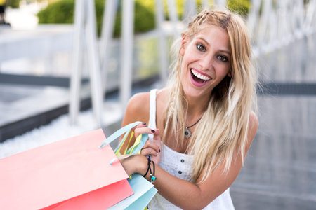 Blonde happy young woman shopping with bags outdoors.