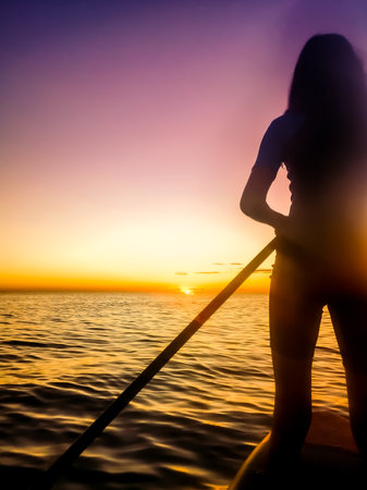 silhouette of a girl practicing paddle surfing in the sea at sunriseの写真素材