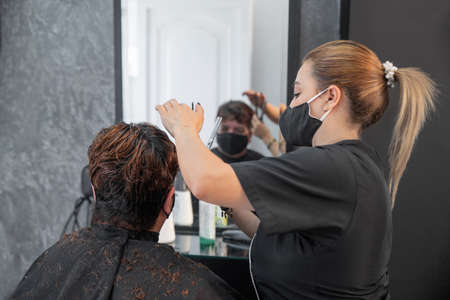 Hairdresser with protective masks cutting hair of womanの写真素材
