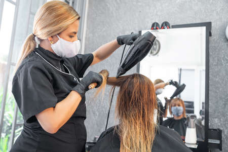 Stylist with protective mask drying hair of a female client at the beauty salonの写真素材