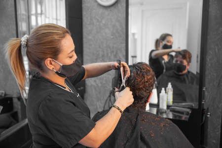 Hairdresser with protective masks cutting hair of womanの写真素材