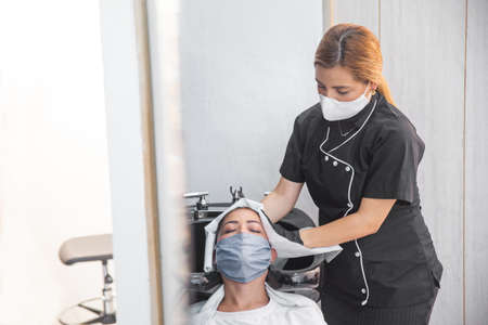 Stylist with protective mask drying the client's hair with a towelの写真素材