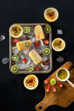 Homemade tropical ice cream garnished with pieces of ice and kiwi, passion fruit and strawberry slices, top viewの写真素材