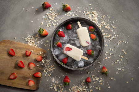 Homemade oats ice cream garnishes with strawberry, oats flakes and pieces of ice on a rustic grayの写真素材