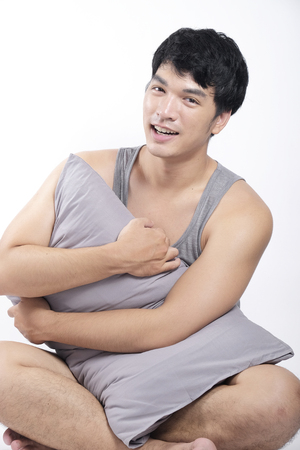 Asian man in grey pajamas sitting and holding the pillowの写真素材