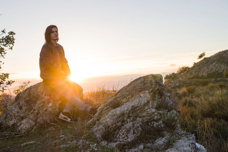 Guy with long hair sitting on a rock.