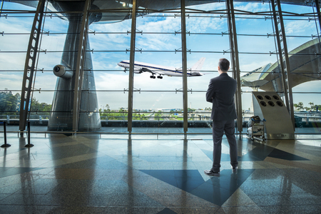 Businessman standing in the airport looking toward outdoor aeroplane with nice skyのeditorial素材