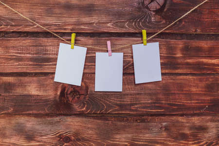 Photo frame made of paper with a clothespin hanging on a rope on a dark wooden background. Mockup for a photo or noteの写真素材