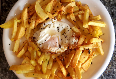 French fries with egg and a little parsley on a white plateの写真素材
