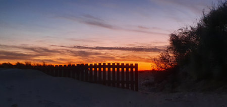 Sunset over the dunes with a wooden fence in the foregroundの写真素材