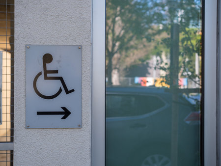 Gray handicap sign on wall outdoors pointing right near entrance