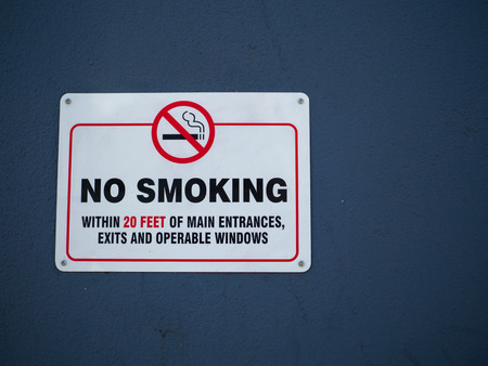 "No smoking within 20 feet of main entrances" sign hanging on a wall outdoorsの写真素材