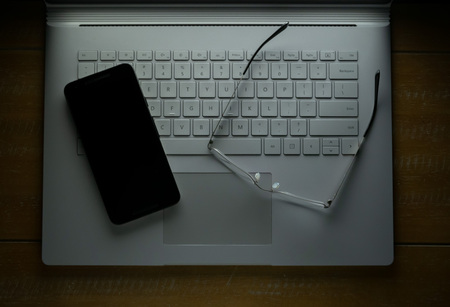 Smartphone and glasses sitting on a laptop in the darkの写真素材