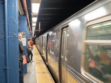 NEW YORK, NY â MAY 18, 2018: Metropolitan Transportation Authority (MTA) subway train whizzing by waiting passengers on 81st street station platformのeditorial素材