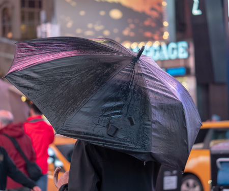Man holds black umbrella reflecting neon advertisement in Times Square, New York Cityの写真素材