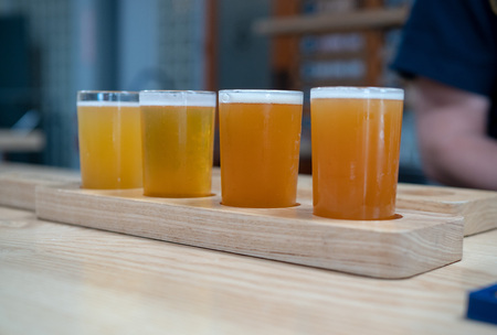 A flight of light colored craft beers sitting on wooden plank on a bar topの写真素材