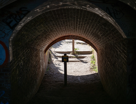 Dark tunnel leading to outdoors with low clearance warning signの写真素材