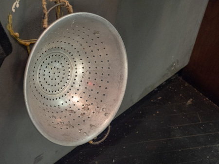 Rusty, stained metal colander hanging on wall with ropeの写真素材