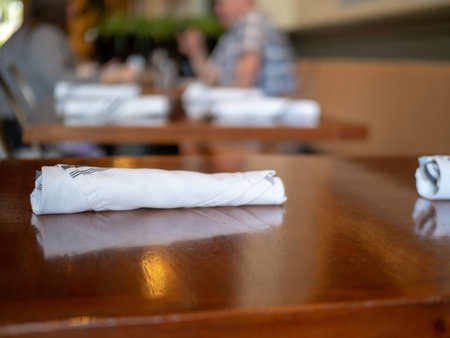 Napkin with utensils inside sitting on restaurant table, patrons in background