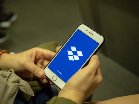Woman opening Dropbox mobile app with logo on iPhone screen while commuting on subway train