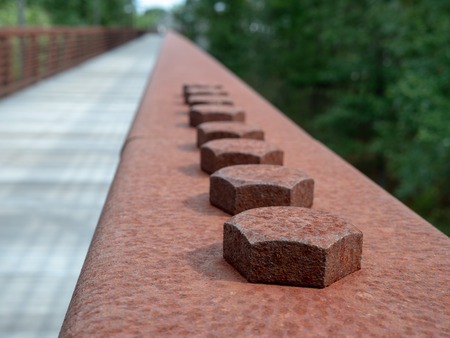 Row of hex screws in a rusted steel handrail on a wooden bridge on hiking pathの写真素材