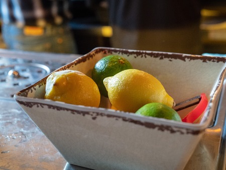 Lemons and limes with peeler sitting in bowl of a bar for bartenders to make cocktailsの写真素材