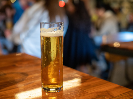 Tall skinny glass of golden lager beer sitting on bar counterの写真素材