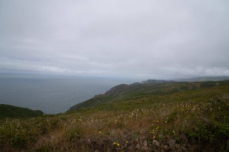 Hills and path leading to endless ocean on cloudy, rainy dayの写真素材