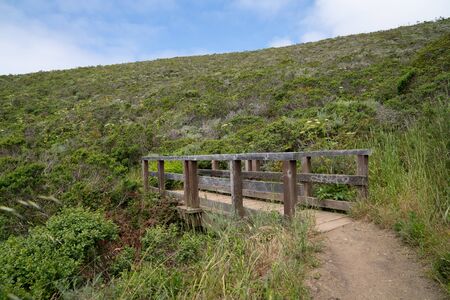 Small wooden bridge on dirt trail path below large hillの写真素材