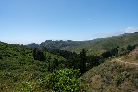 Blue skies, grassy hills, man on hiking path, city in backgroundの写真素材