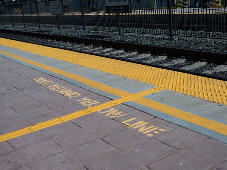 Wait behind yellow line warning on ground on train platformの写真素材